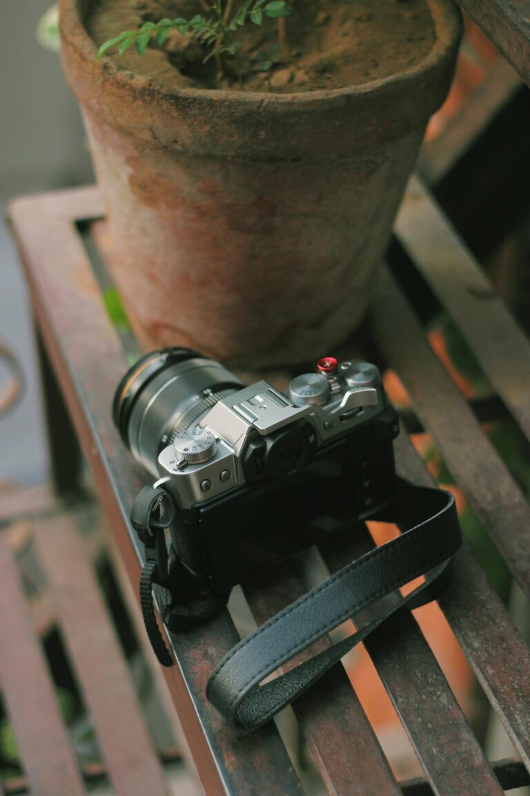 A camera lies on a metal bench beside a clay pot with a plant, creating an artful and rustic scene.