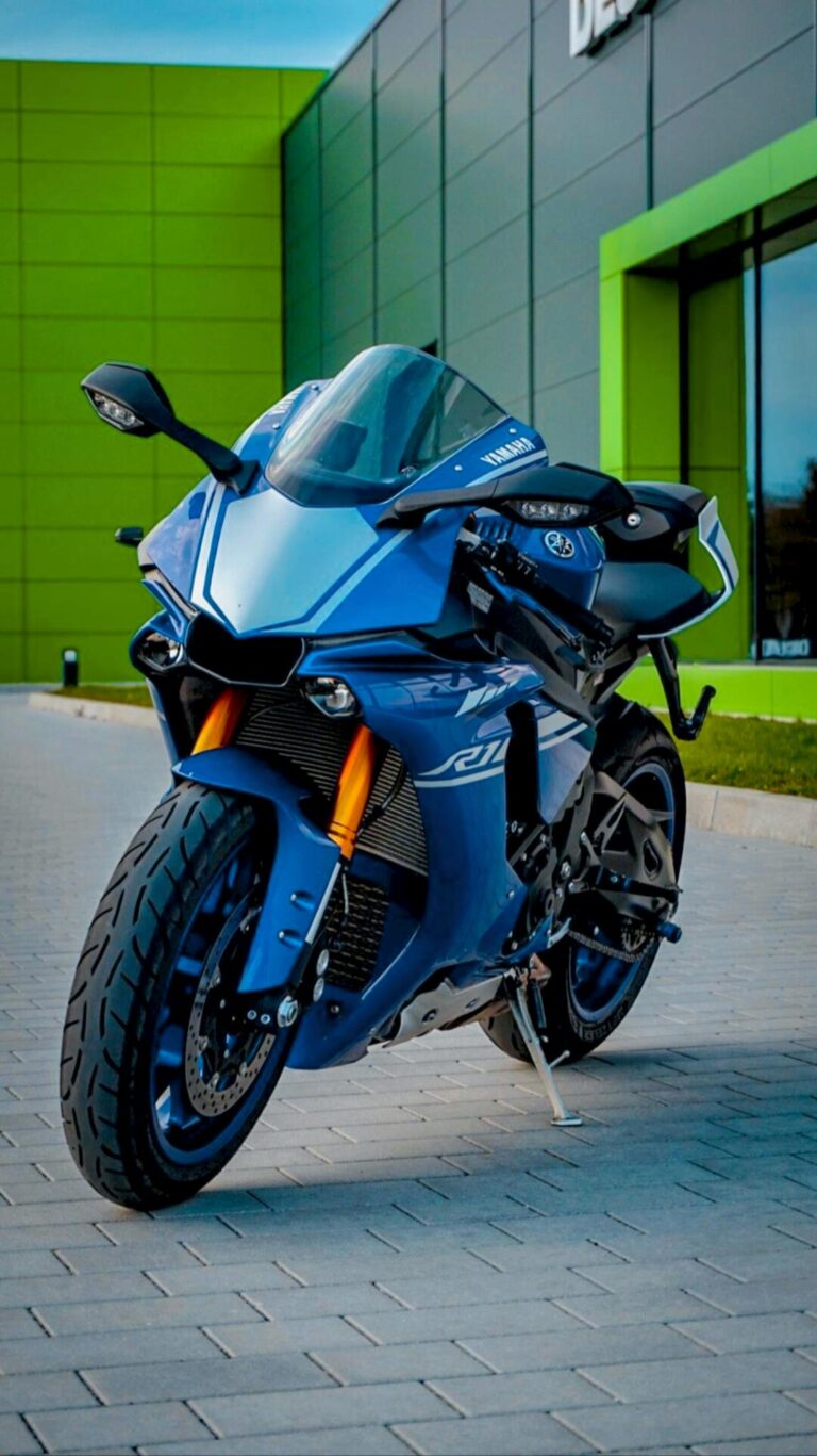 A sleek blue sports motorcycle parked outdoors with a modern architectural backdrop.
